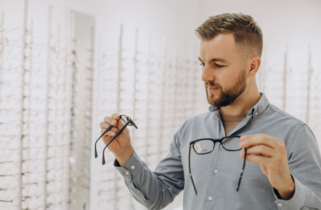 A man examining two distinct pairs of glasses to carefully compare their features.