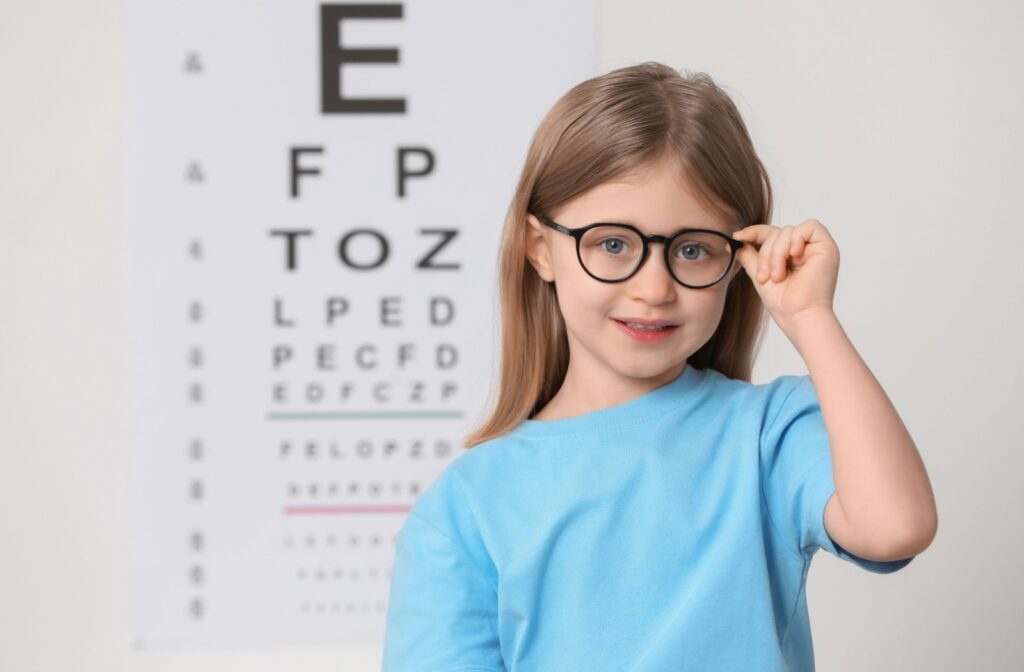 A child wearing glasses stands in front of an eye chart.