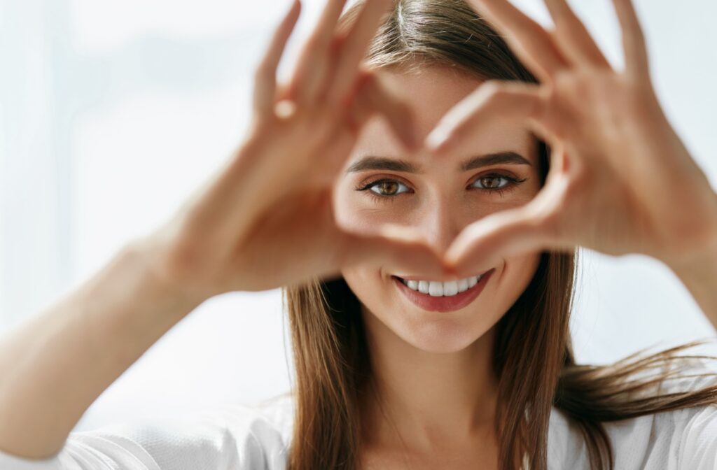 A person forms a heart shape with their hands in front of their vibrant, healthy eyes.