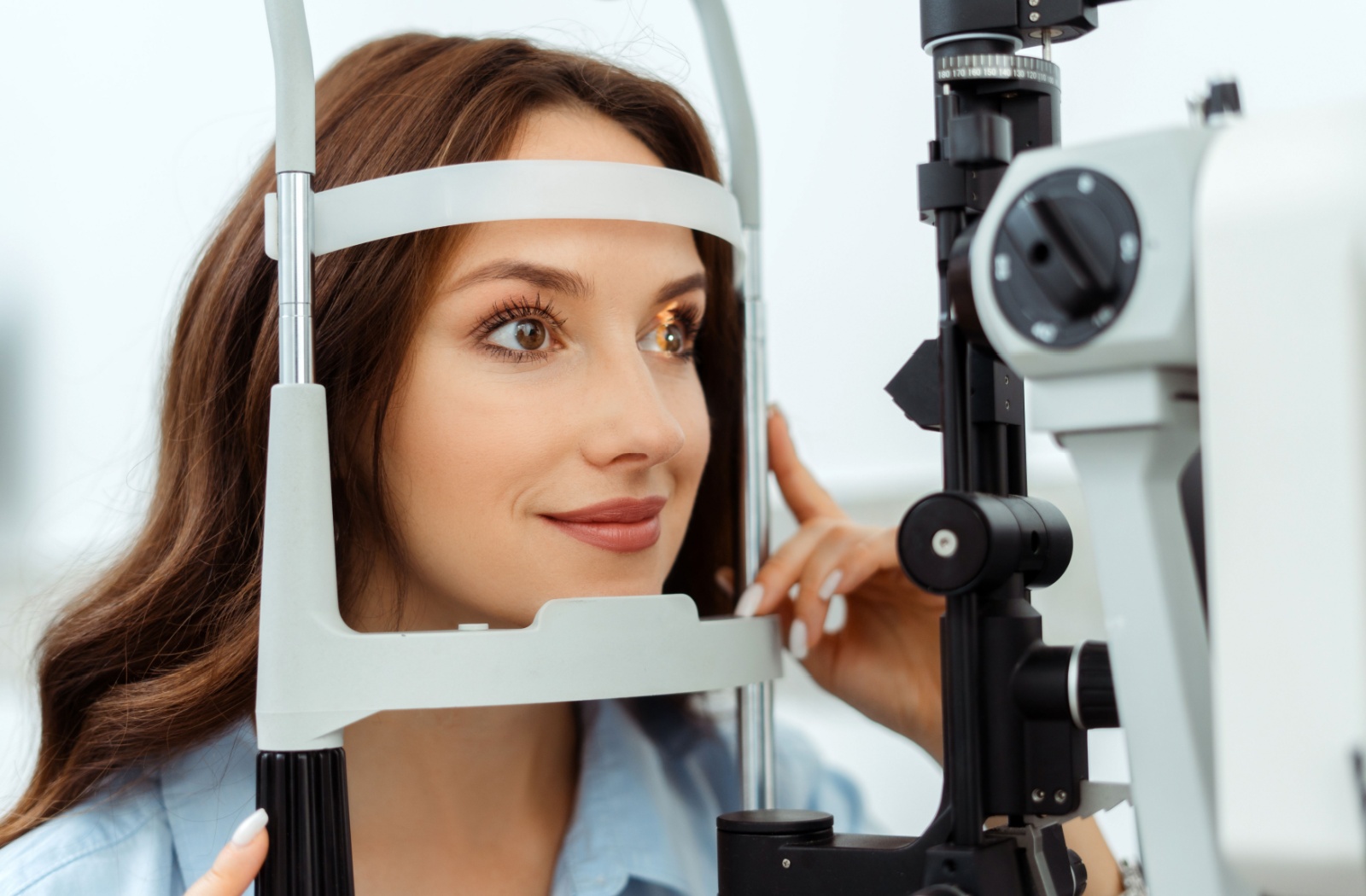 Adult patient smiling while undergoing a comprehensive annual eye exam with a diagnostic laser device.