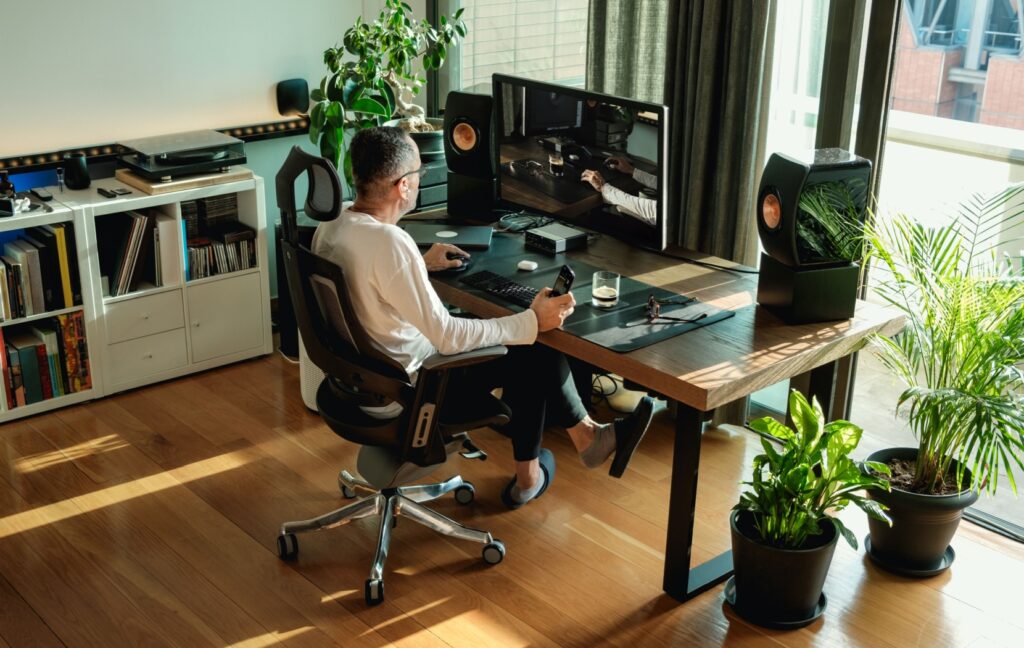 A person sits with proper posture at their desk. The room is well lit to reduce eye strain during the work day.