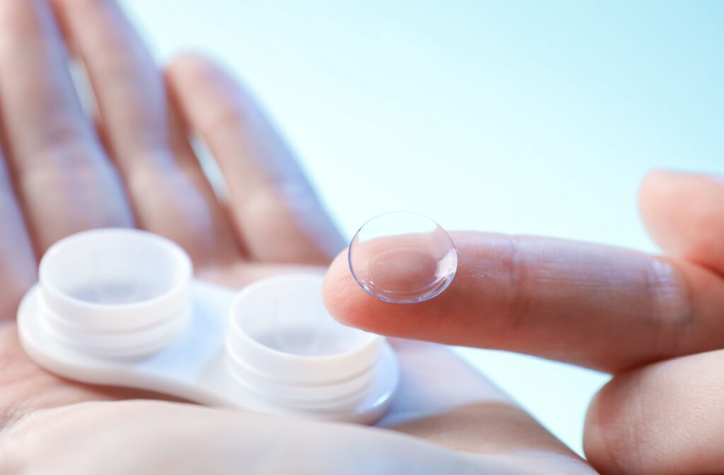 A hand holding a contact lens case while showing a close up of a contact lens.