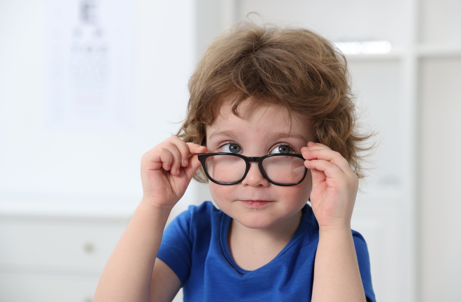 A young kid looking over top of the glasses on their face